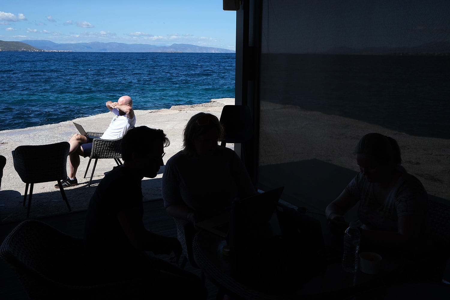 Fotografi av Fiken-ansatt som sitter i sola i syden, med en bærbar PC i fanget.